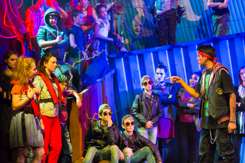 Young performers gathered closely in a blue-lit scene from a London Youth Opera production.
