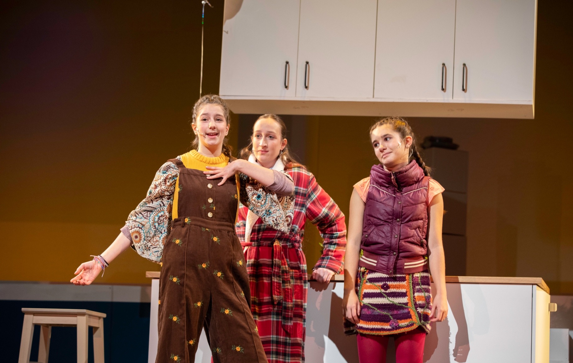 Three friends from the village of Middle Demos gather around a kitchen counter in warm autumnal clothes, mid-conversation.